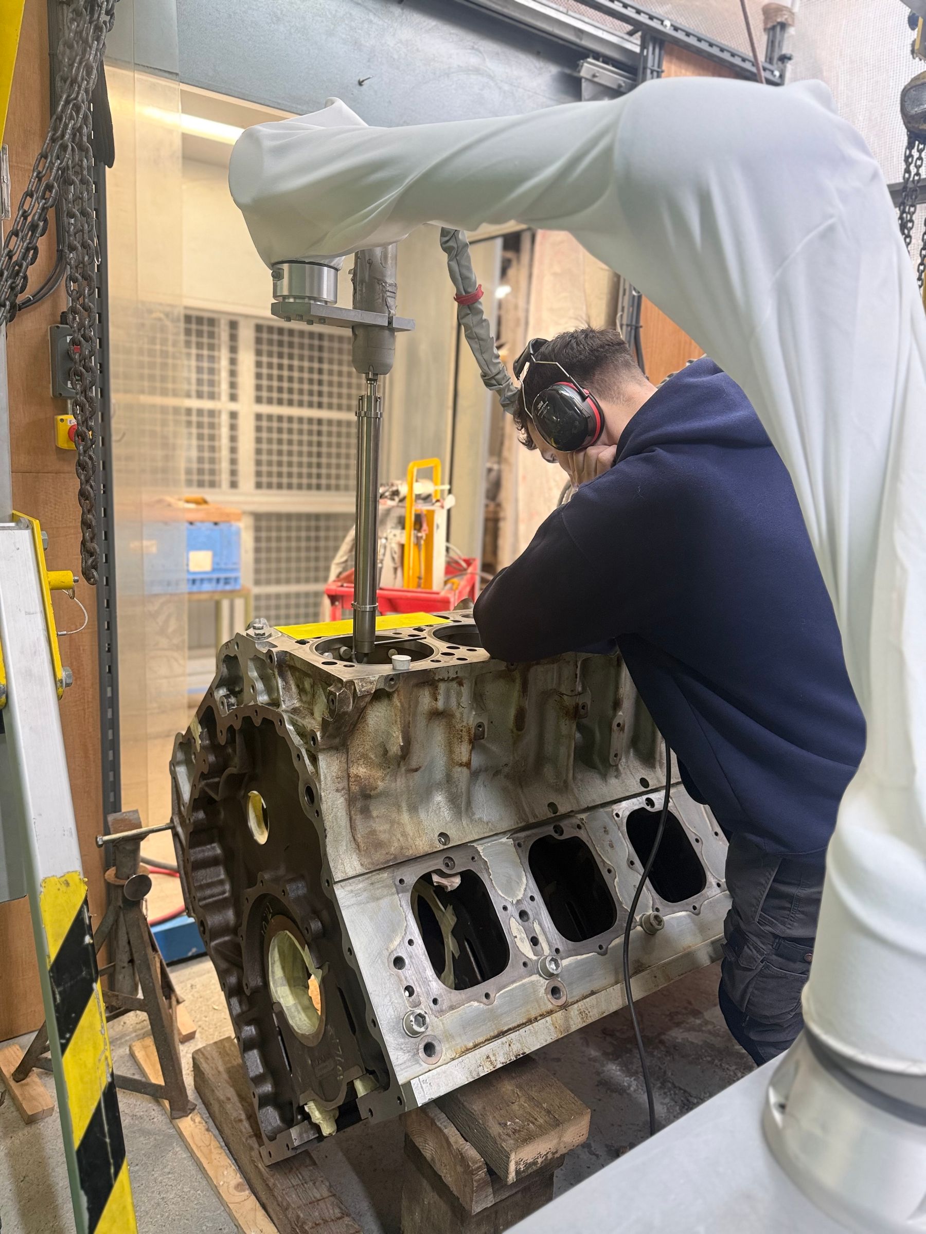 Technician operating cold spray robot arm on V12 engine block